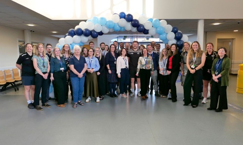 Picture of St James Staff stood in font of a balloon arch just before we welcome families into the building.
